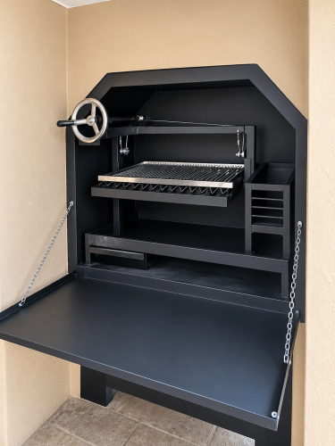 Black built-in Parrilla braai with adjustable stainless steel cooking grid, handwheel and fold-down front door